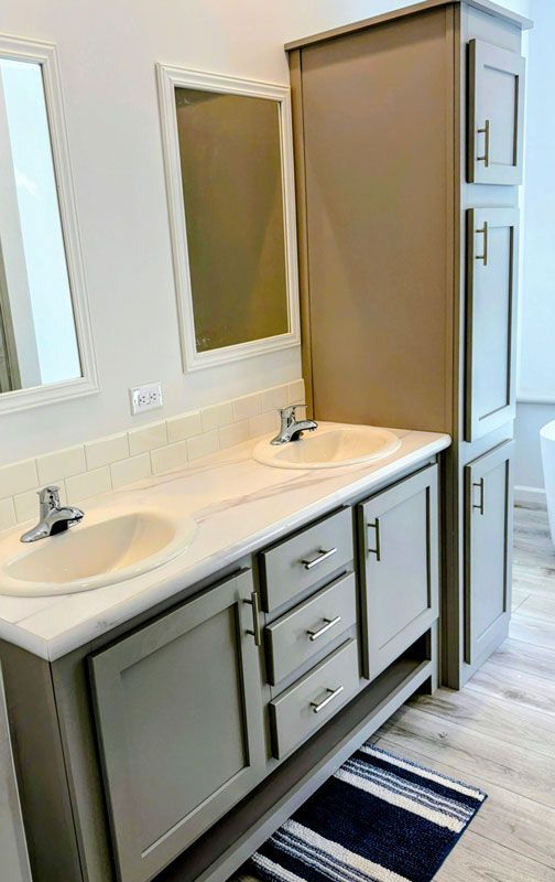 Bathroom vanity with double sinks, gray cabinets, mirrors, and a tall storage cabinet