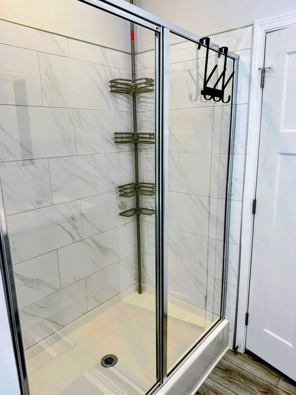 Glass shower stall with white tile walls and built-in corner shelves in a bathroom