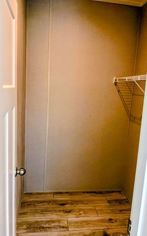 Empty walk-in closet with beige walls, wood-look floor, and white wire shelving on the right.