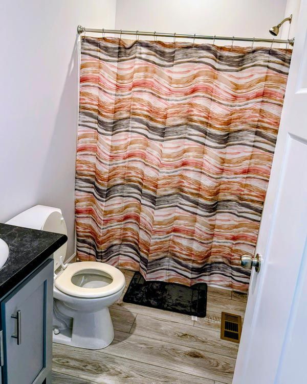 Small bathroom with a toilet, sink, and wavy multicolor shower curtain.