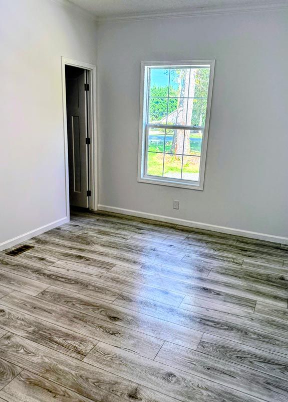 Empty room with gray wood flooring, white walls, and a window letting in daylight.