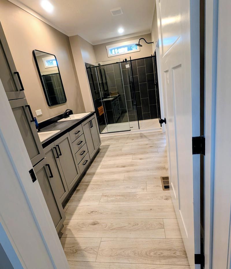 Narrow modern bathroom with double vanity, black shower enclosure, and light wood flooring