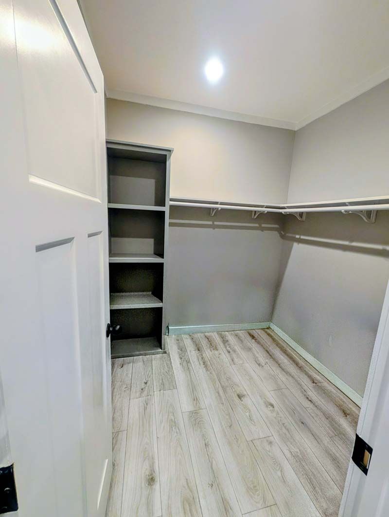 Empty walk-in closet with white walls, built-in shelving, hanging rods, and light wood flooring.
