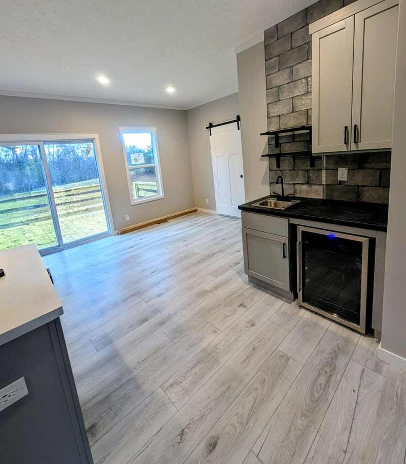 Bright open kitchen with light wood floors, white cabinets, gray stone backsplash, and sliding glass doors.