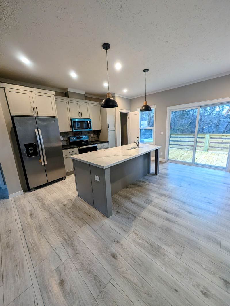 Modern kitchen with gray island, stainless appliances, pendant lights, and large sliding glass doors.