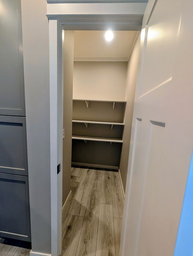 Small walk-in closet with shelves and wood-look flooring, viewed through an open doorway.