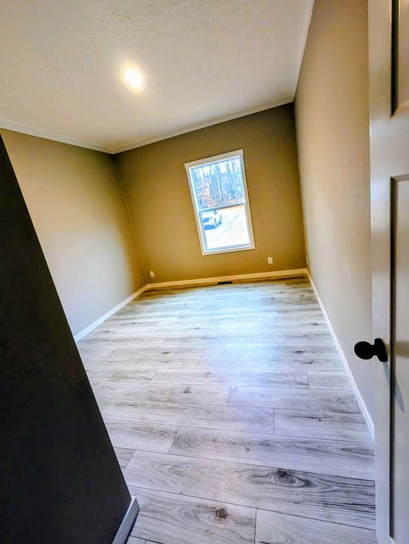 Empty beige bedroom with white wood-look floors and a single window.