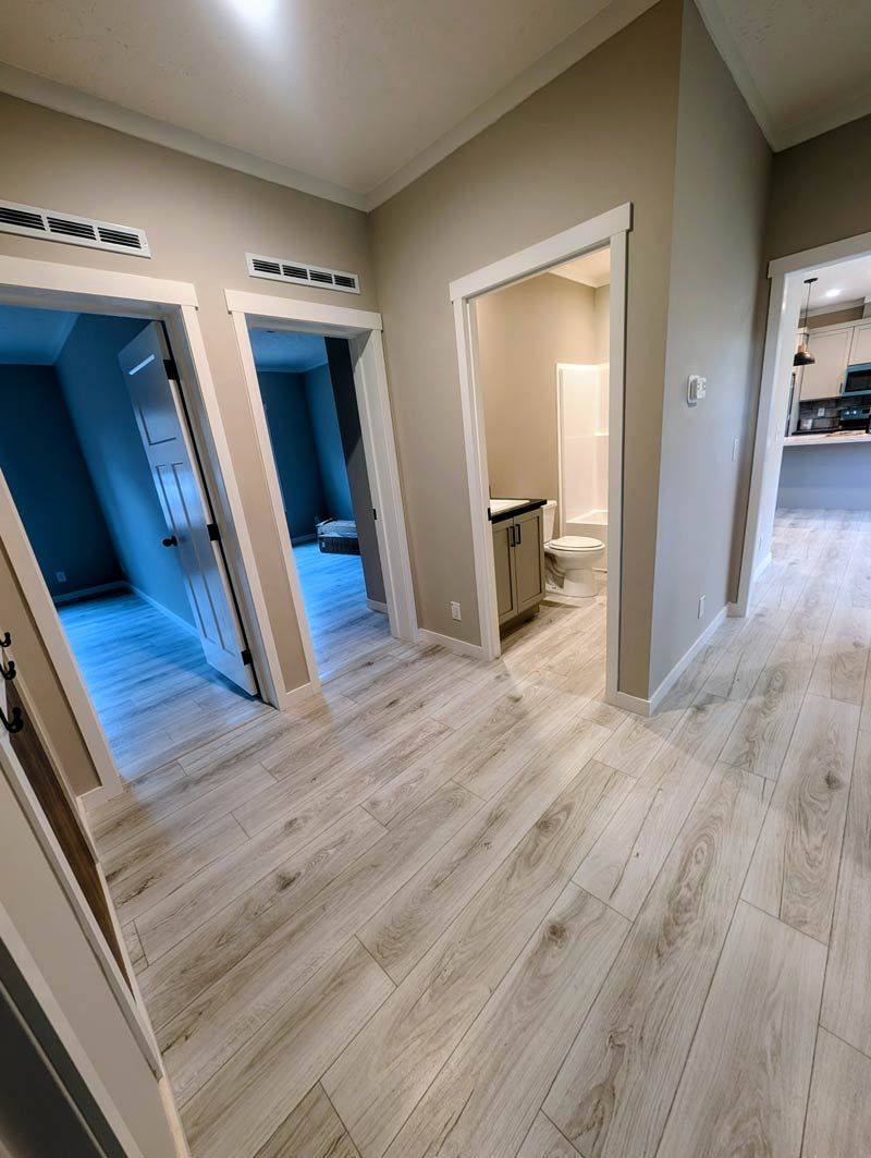 Empty hallway with light wood floors, beige walls, and three open doorways in a home