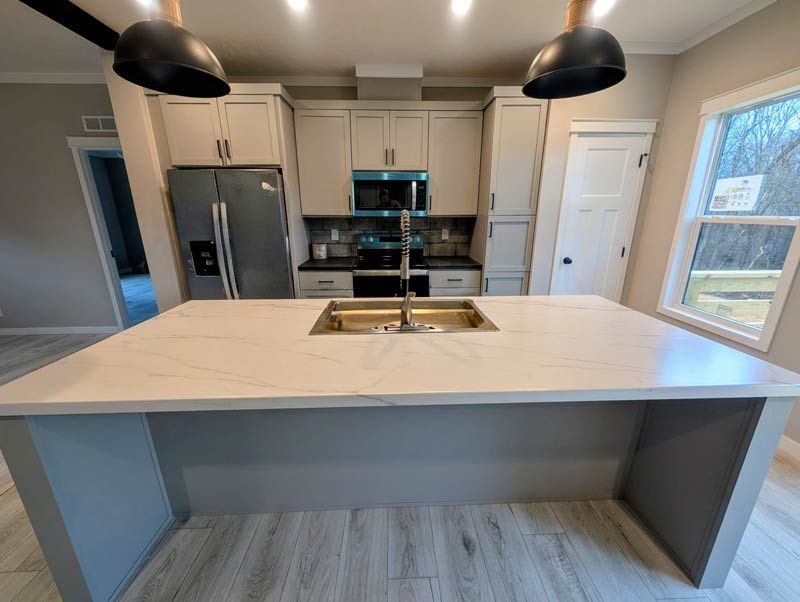 Modern kitchen with white island, pendant lights, stainless appliances, and large window