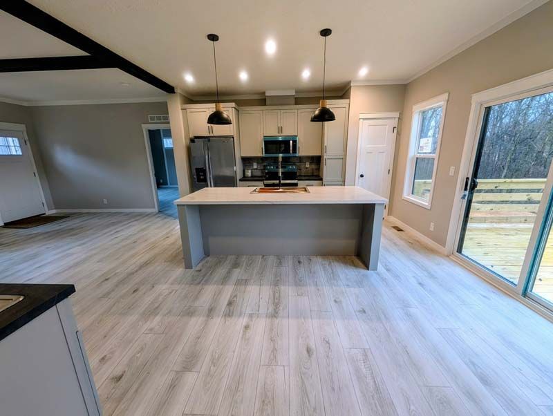 Modern open-concept kitchen and living space with island, pendant lights, wood floors, and sliding glass doors