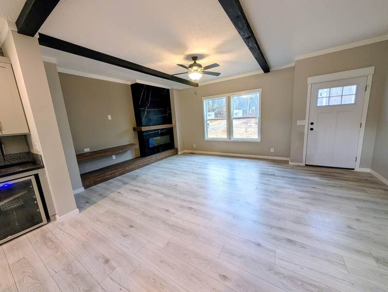 Spacious living room with light wood floors, ceiling fan, built-in shelves, fireplace, and white front door.