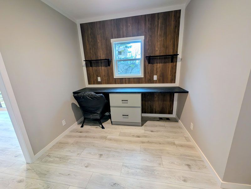Small home office with a desk, chair, drawers, and a window on a wood accent wall.