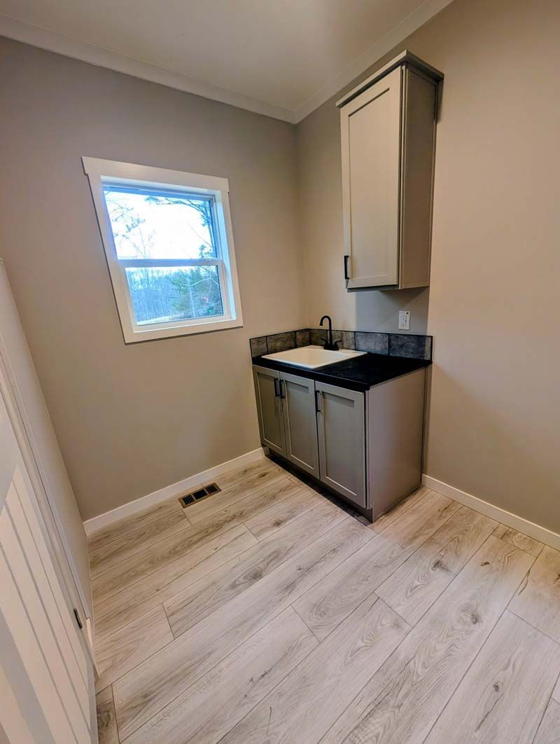 Small beige laundry room with stacked washer-dryer, window, and white wood-look floor