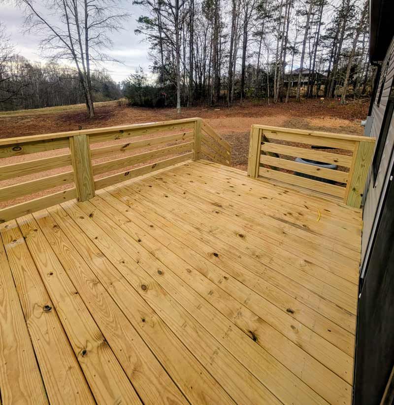 Wooden deck with railing overlooking a wooded backyard in winter under cloudy skies