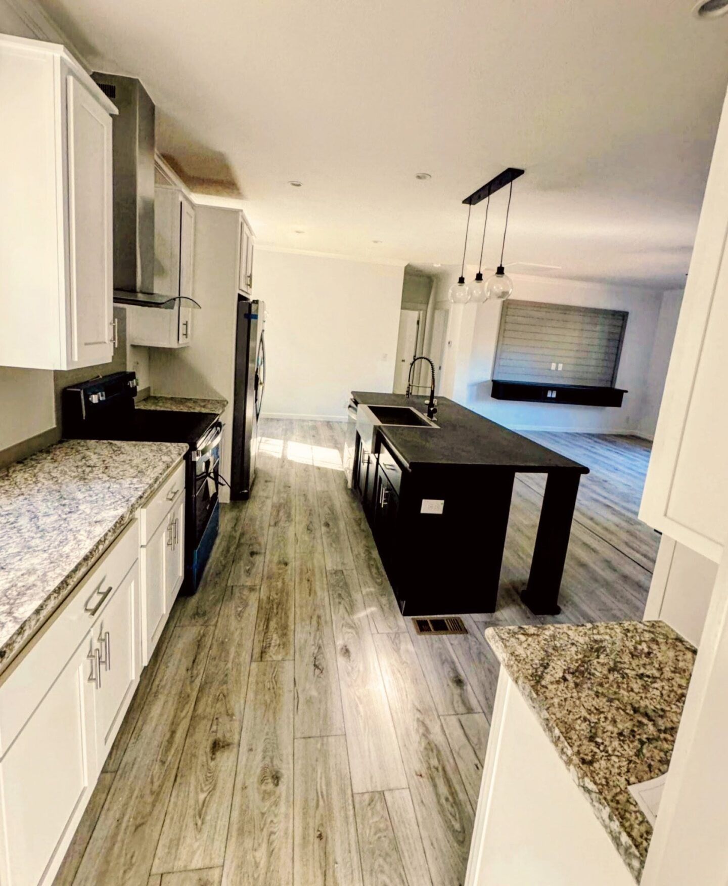 Modern kitchen with granite counters, dark island, and open view to a dining/living area.