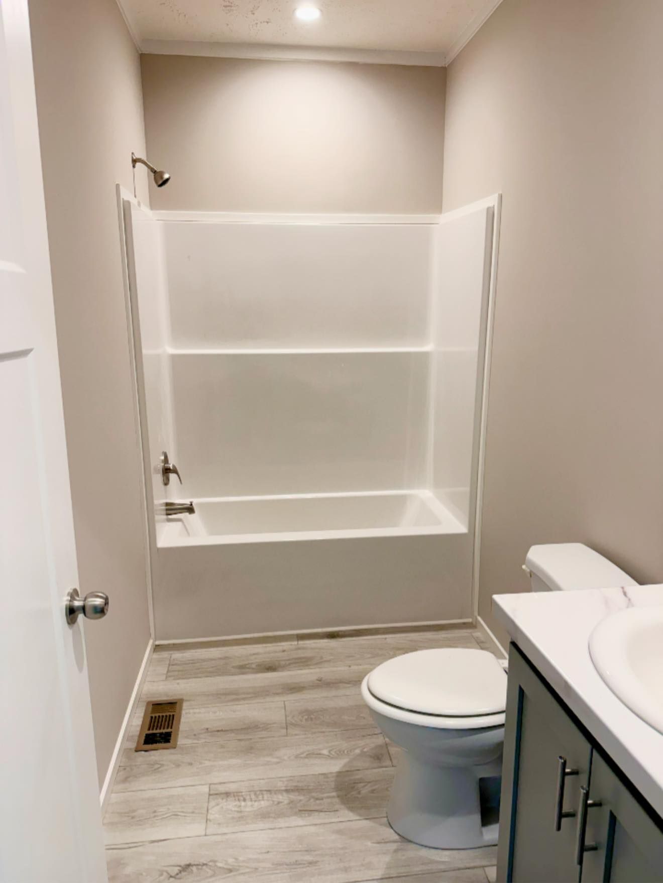Small bathroom with a tub-shower, toilet, vanity sink, and light wood flooring.