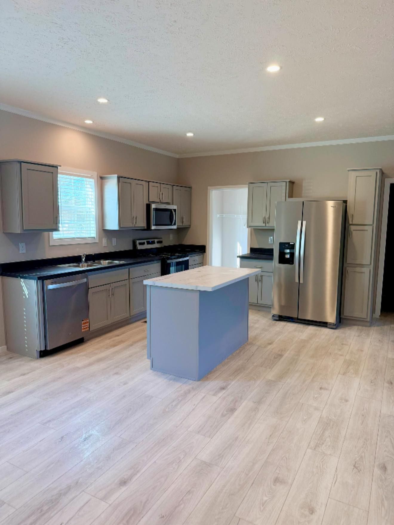 Modern kitchen with stainless steel appliances, gray cabinets, island, and light wood flooring