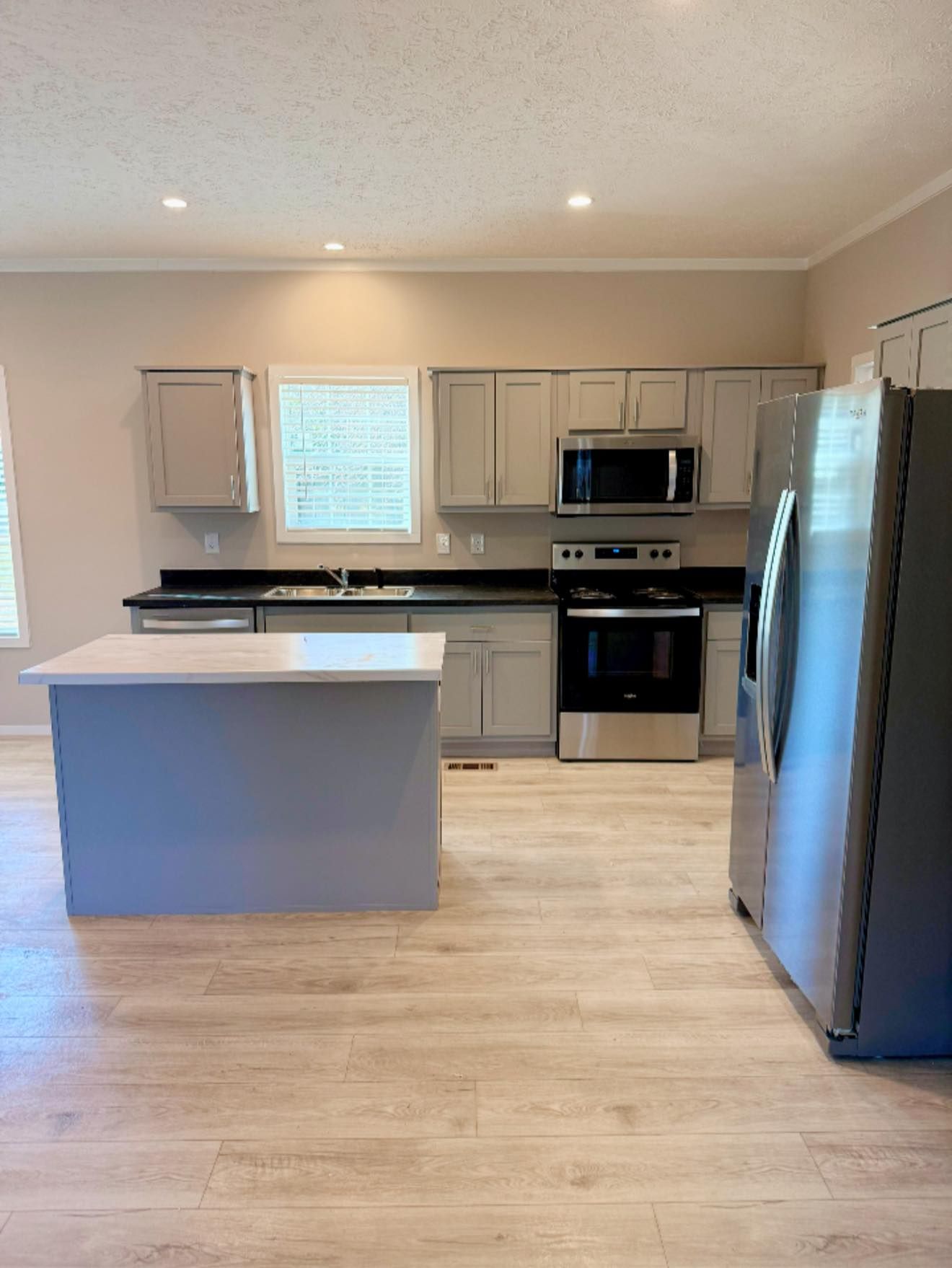 Modern kitchen with gray cabinets, white island, stainless appliances, and wood-look flooring.