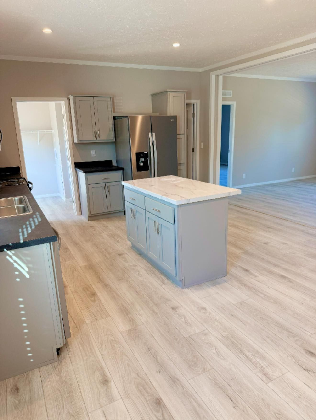 Empty modern kitchen and living area with light wood floors, white cabinets, and a gray island.