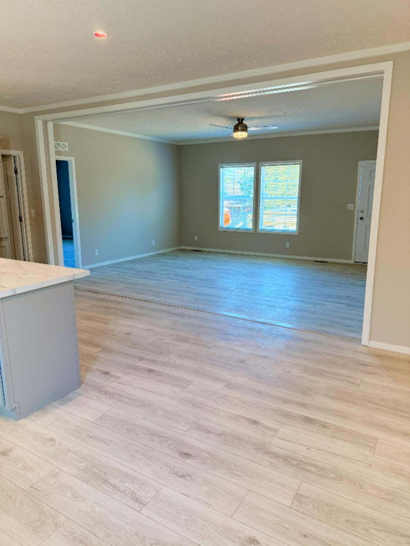 Empty open-plan living room with light wood floors, gray walls, and a ceiling fan