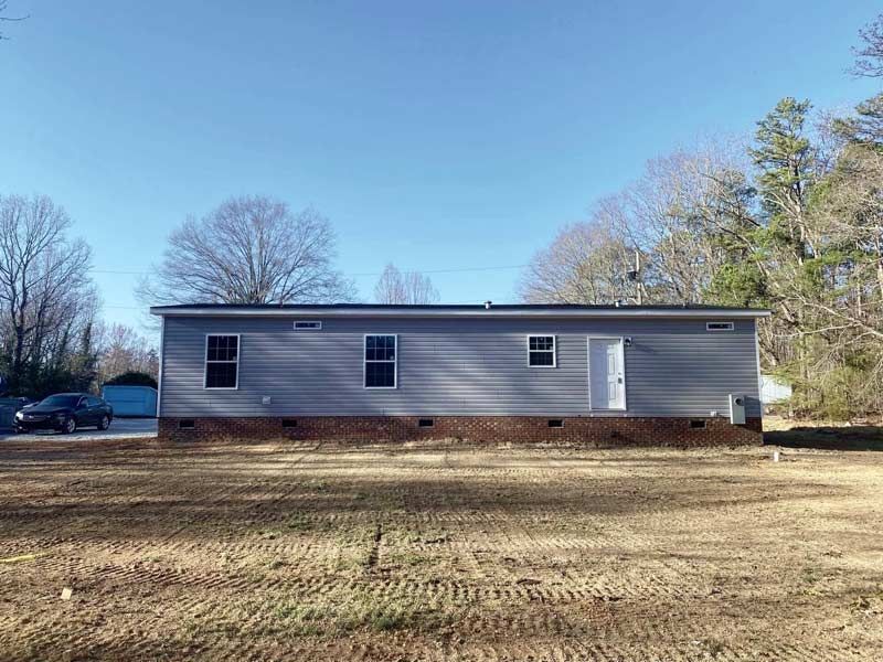 Single-story gray house with a brick foundation in a grassy yard under a clear blue sky