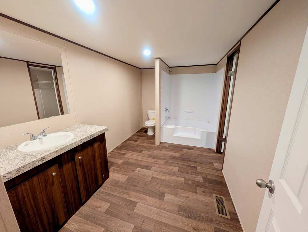 Long, narrow bathroom with wood vanity, granite countertop, toilet, and shower alcove