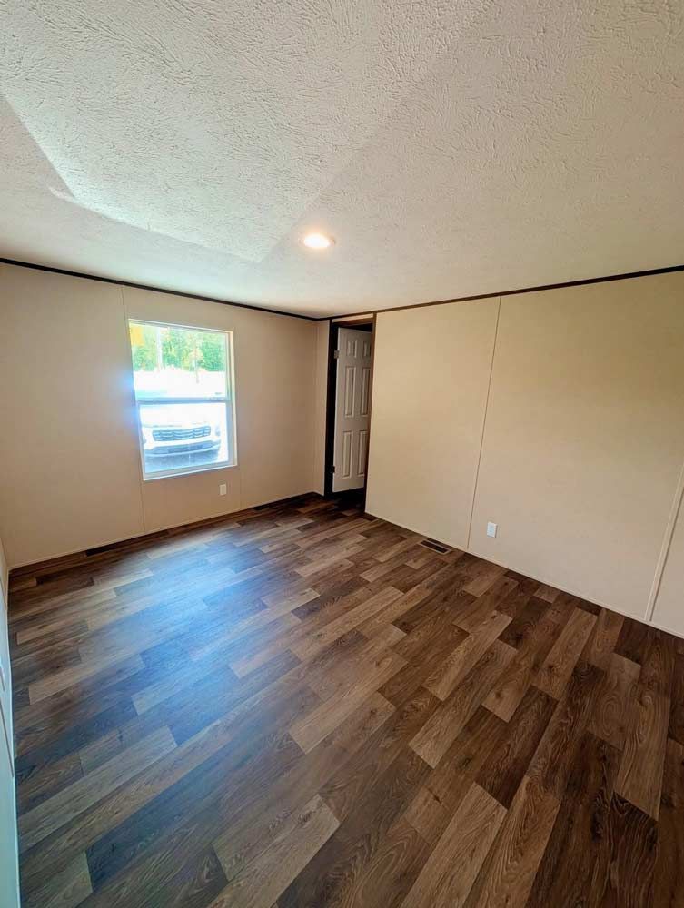 Empty unfurnished room with wood-pattern floor, white walls, window, and open doorway.
