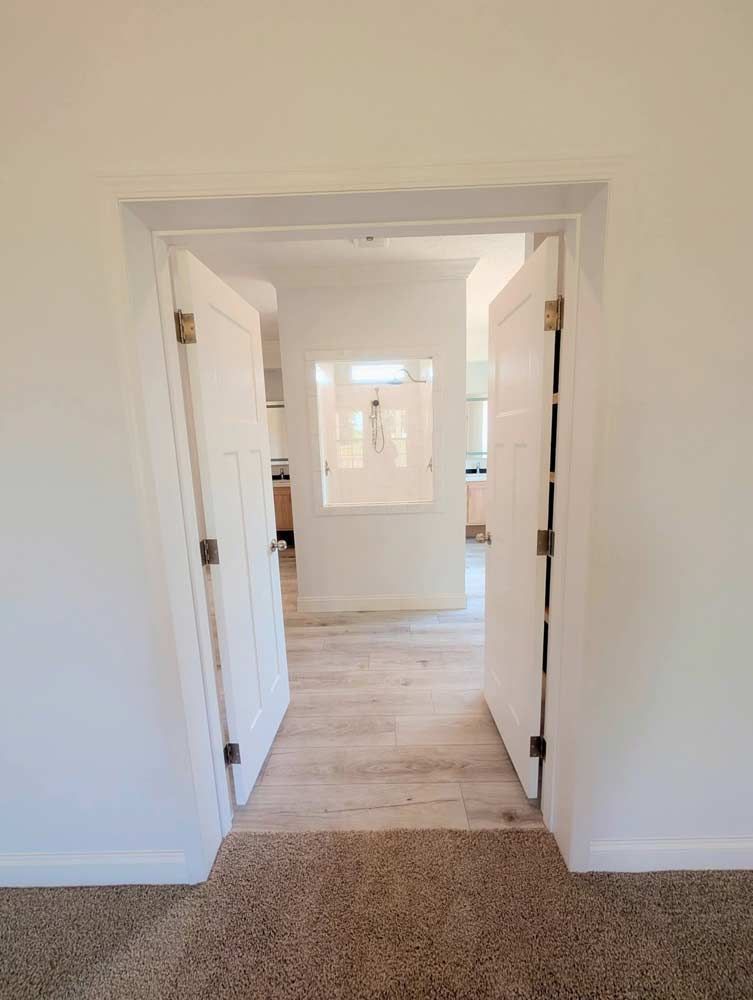 Hallway view through open white double doors into a bright room with light wood flooring