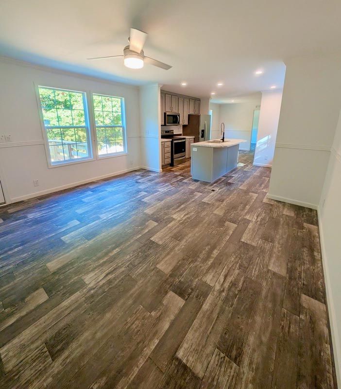 Bright open kitchen and living area with wood-look floors, white cabinets, island, and large windows