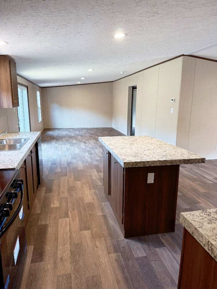 Empty modern kitchen and living area with wood floors, island counters, and large windows