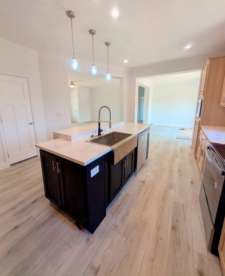 Bright modern kitchen with island, dark cabinets, light wood floors, and pendant lights