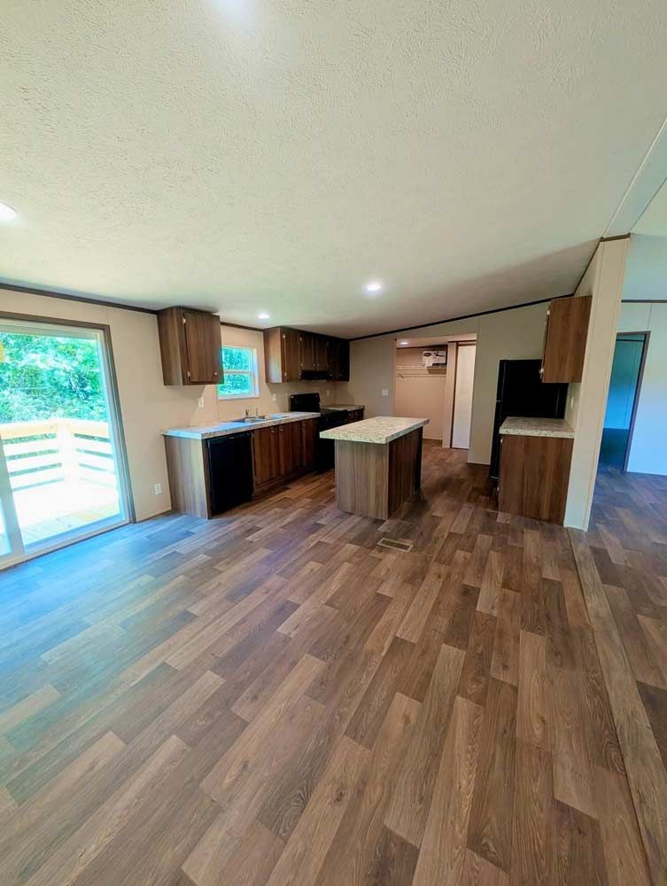 Empty modern kitchen and dining area with wood floors, island, cabinets, and sliding glass door to patio