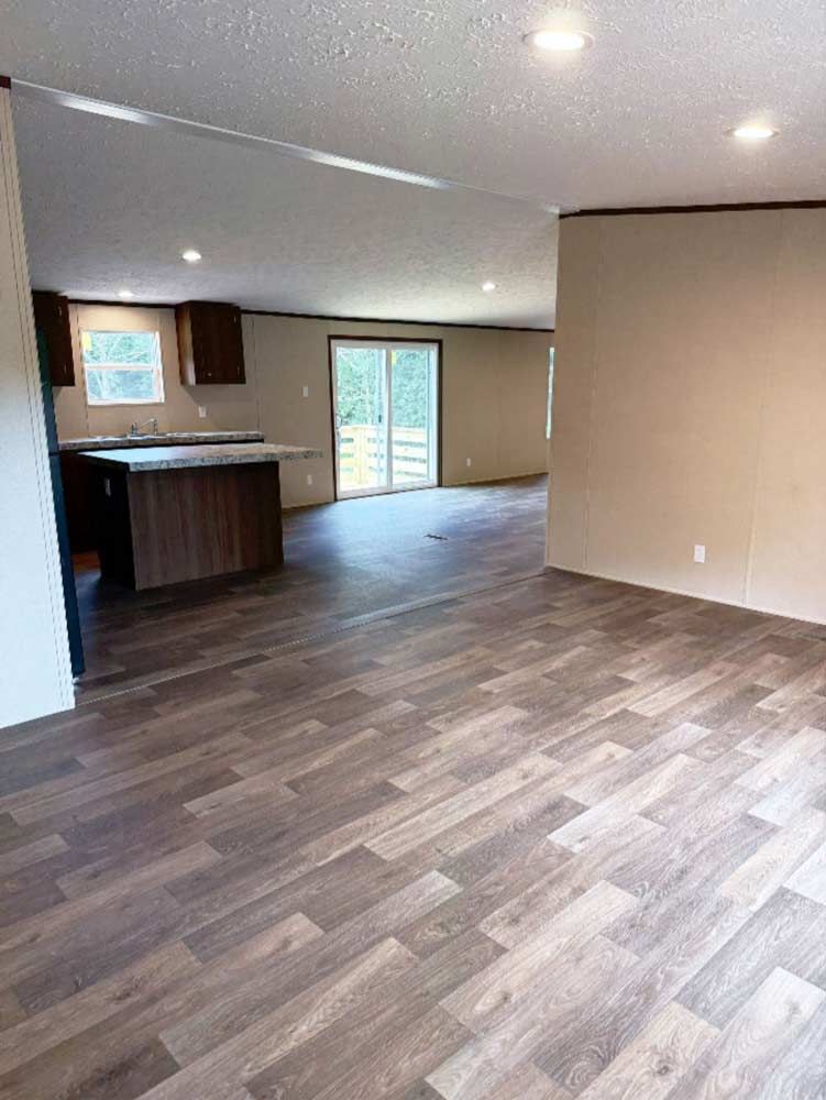 Empty open-plan living room with wood-patterned flooring, neutral walls, and sliding glass doors.