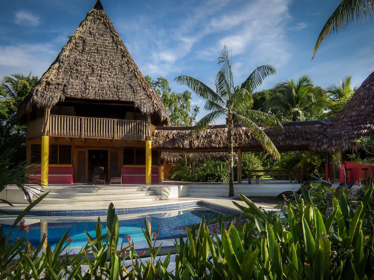 Thatched tropical resort building with pool, palm trees, and blue sky