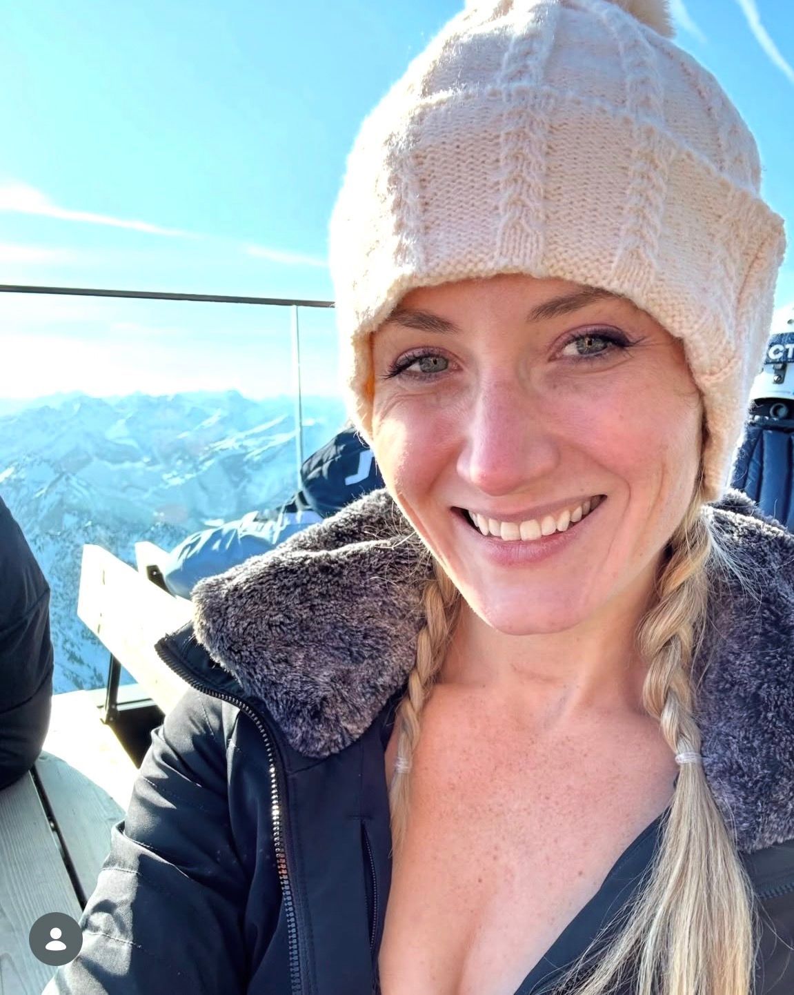 Lauren in a white knit hat on a snowy mountain with bright blue sky behind her