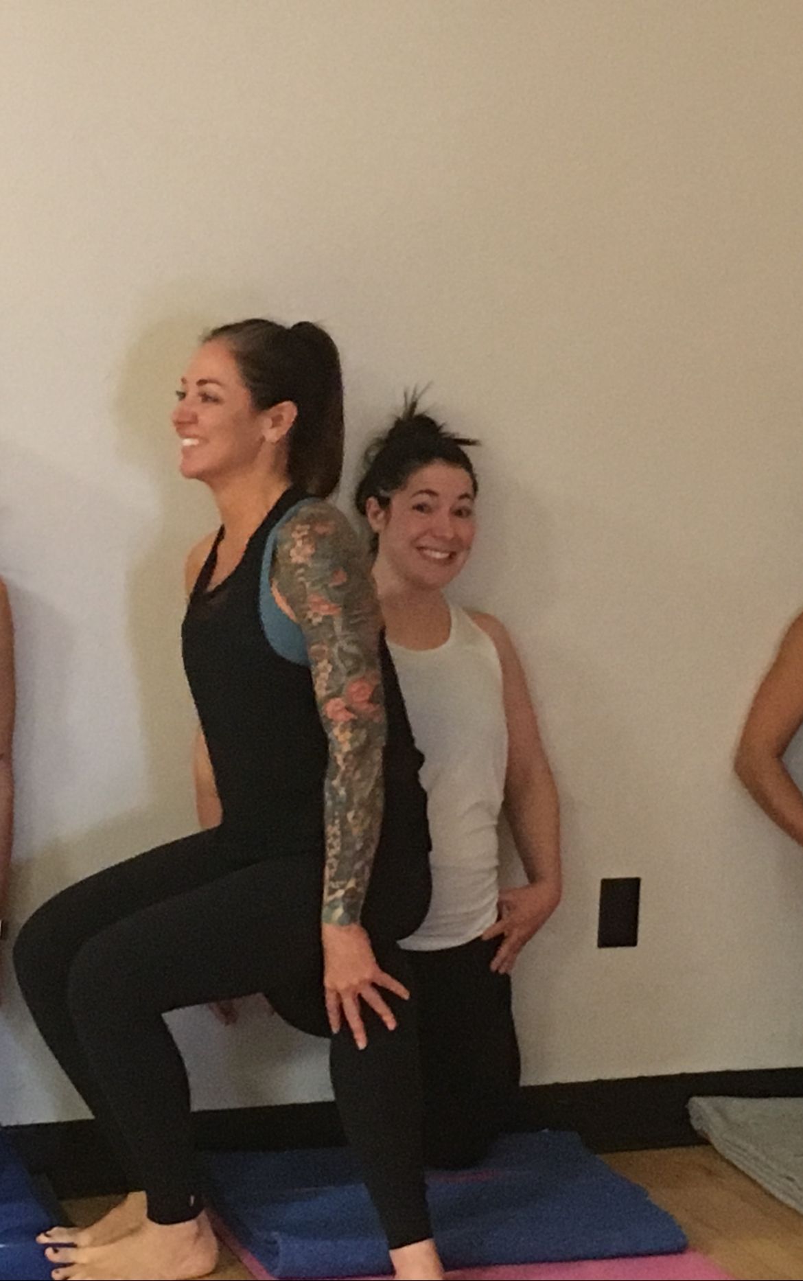 Two women doing a yoga pose on mats against a plain wall