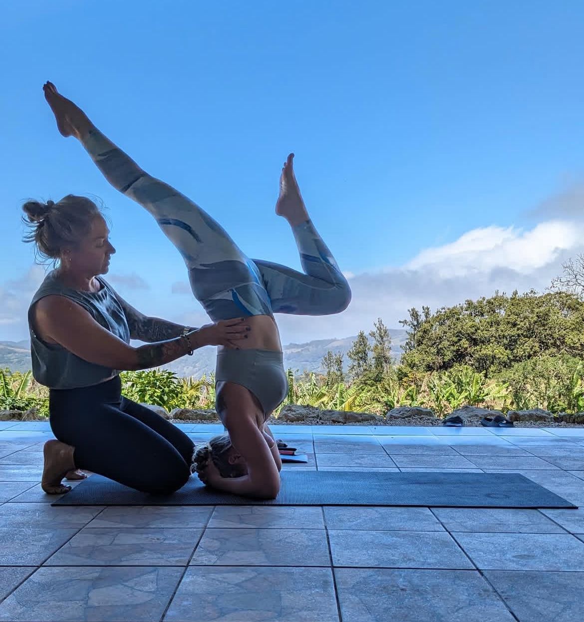 Two people practicing acro yoga on a deck with a tropical ocean view