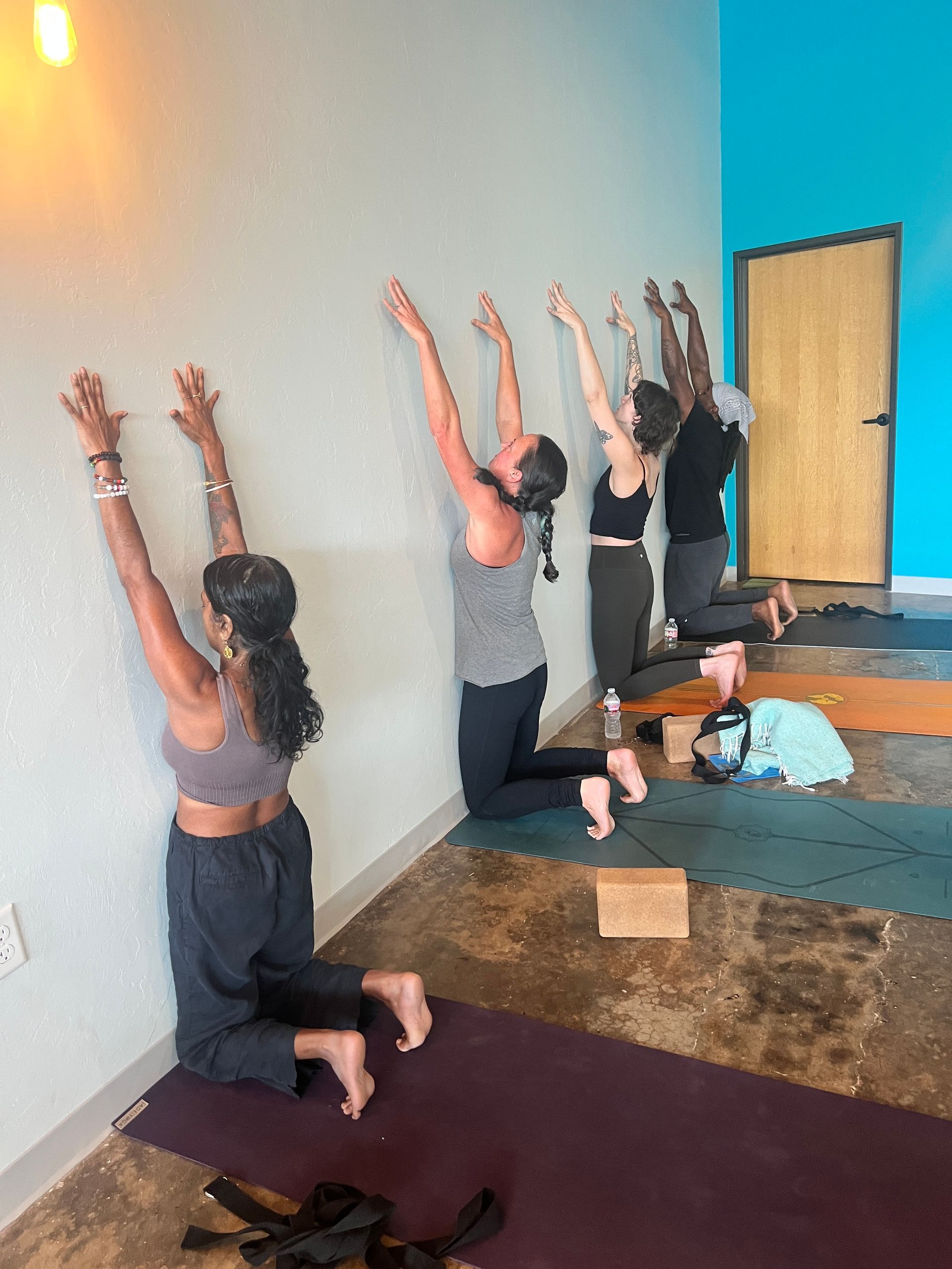 People kneeling with arms raised in a yoga/stretch class on mats in a studio