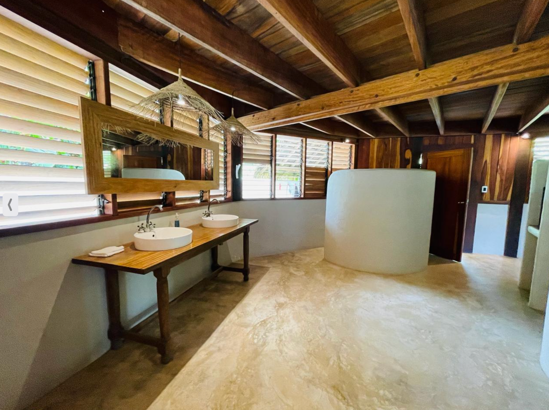 Rustic bathroom interior with double sink, mirror, toilet, and slanted wood-beam ceiling