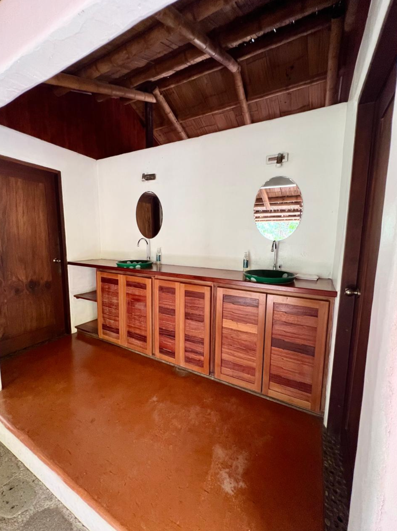 Wood-paneled room with a long wooden cabinet, two oval mirrors, and a sloped ceiling.