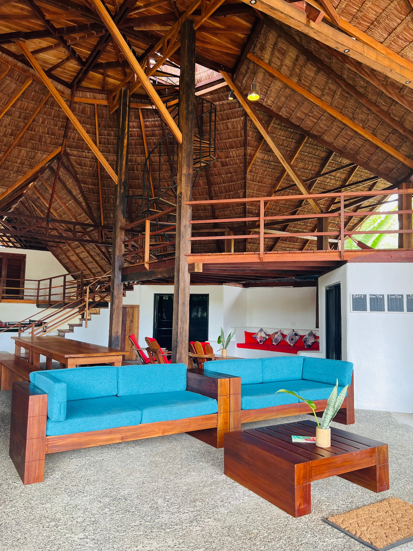 Thatched-roof lounge with turquoise sofas, wooden tables, and a mezzanine in an open-air resort seating area