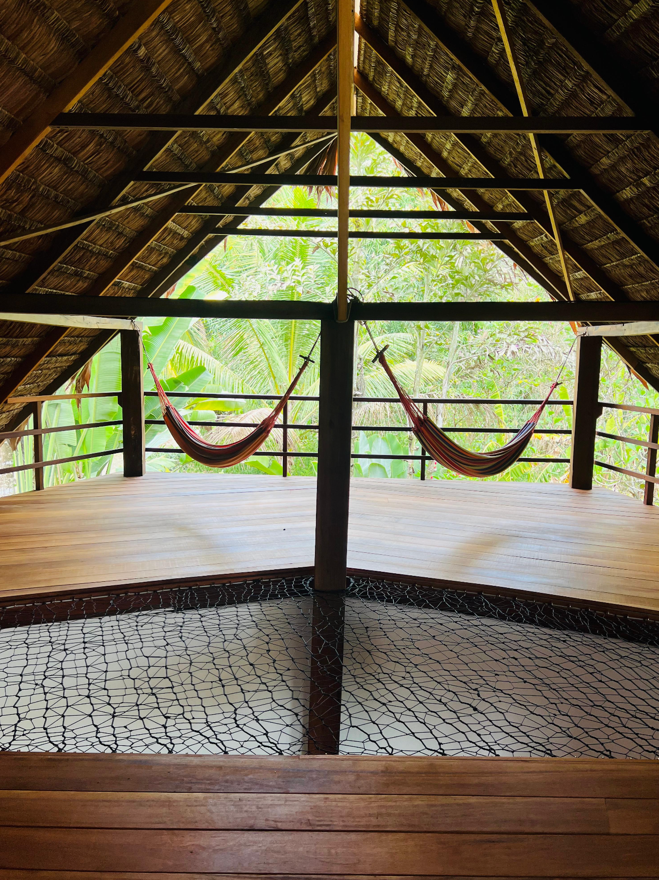 Open-air wooden pavilion with hammocks, thatched roof, and tropical greenery beyond the balcony.