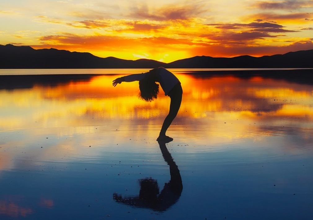 Silhouette of a dancer at sunset reflected on calm water beneath a colorful sky