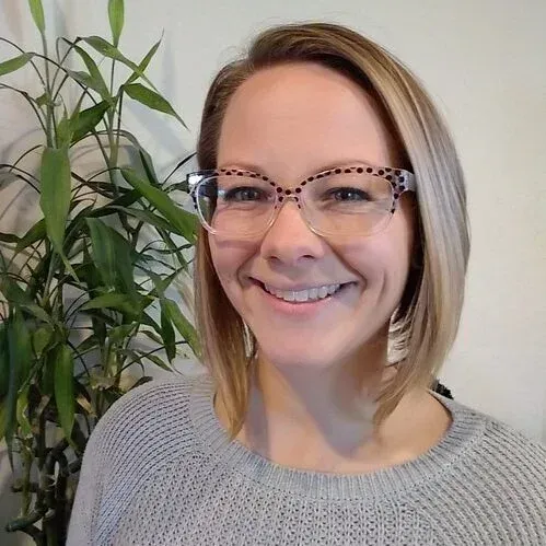Katie Dautrich wearing glasses beside a leafy houseplant, indoors.