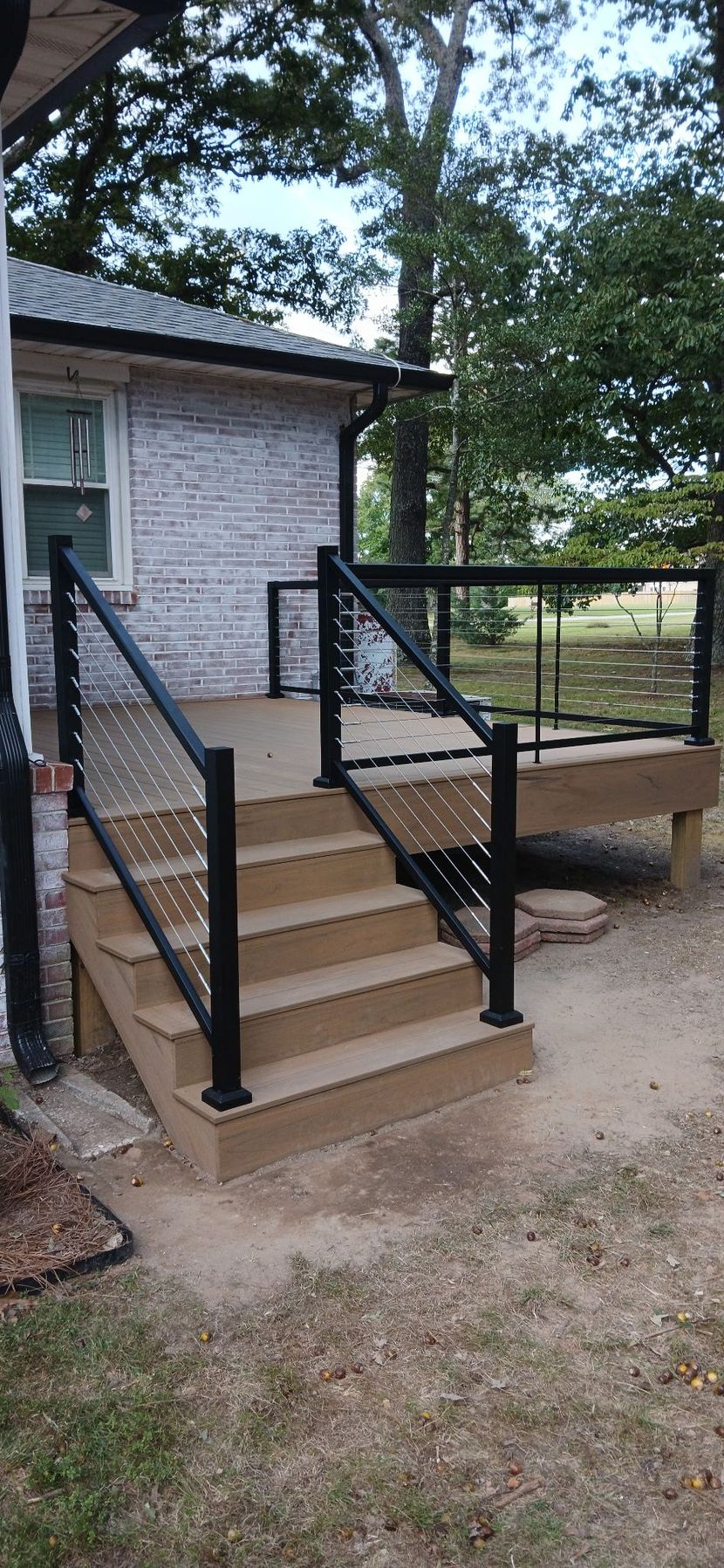 A wooden deck with black railing leads up to a deck and the entrance of a building with stone siding.