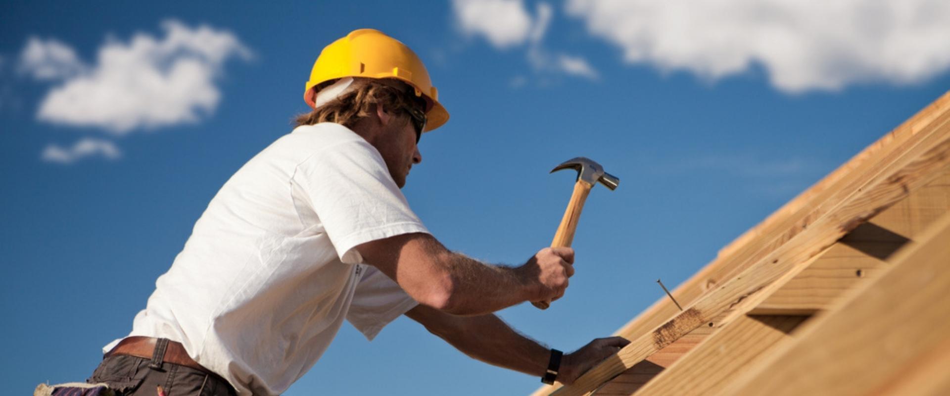 Ein Mann mit Schutzhelm arbeitet mit einem Hammer auf einem Dach.