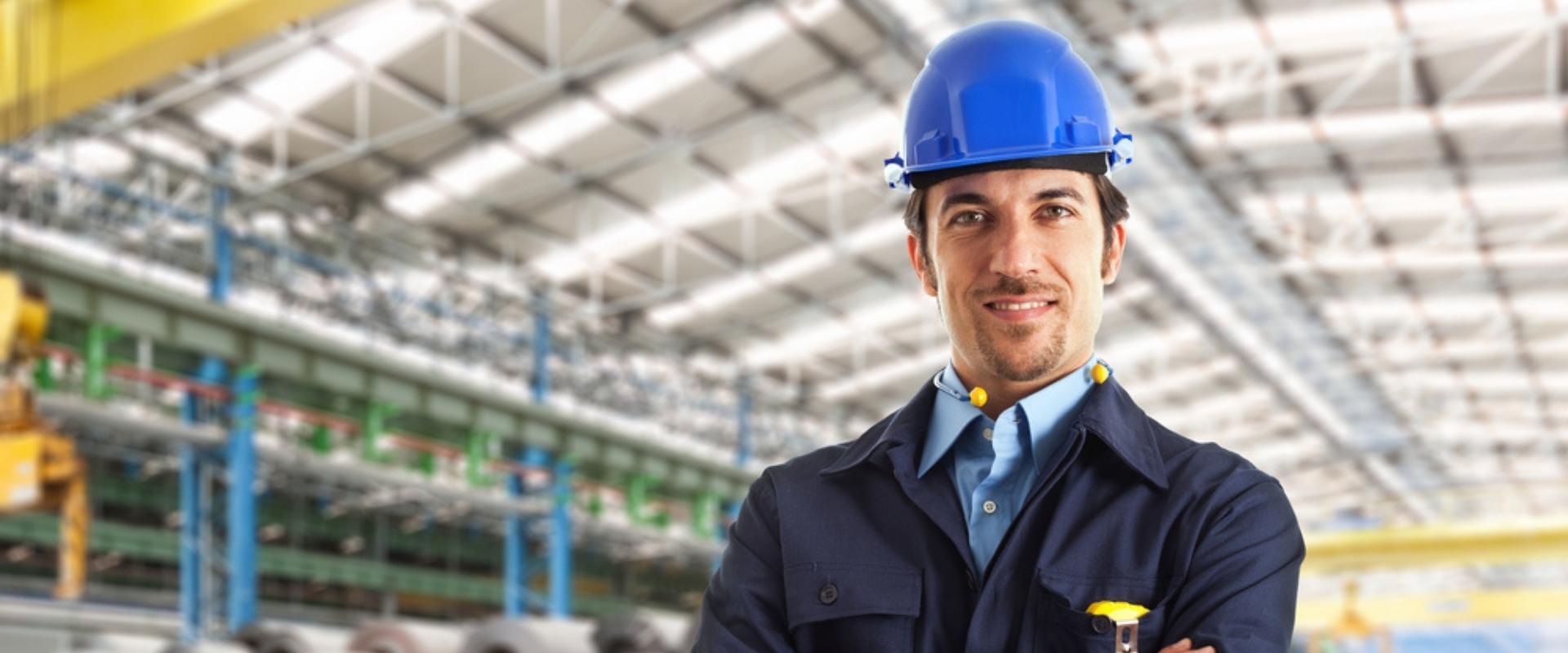 Ein Mann mit Schutzhelm steht mit verschränkten Armen in einer Fabrik.