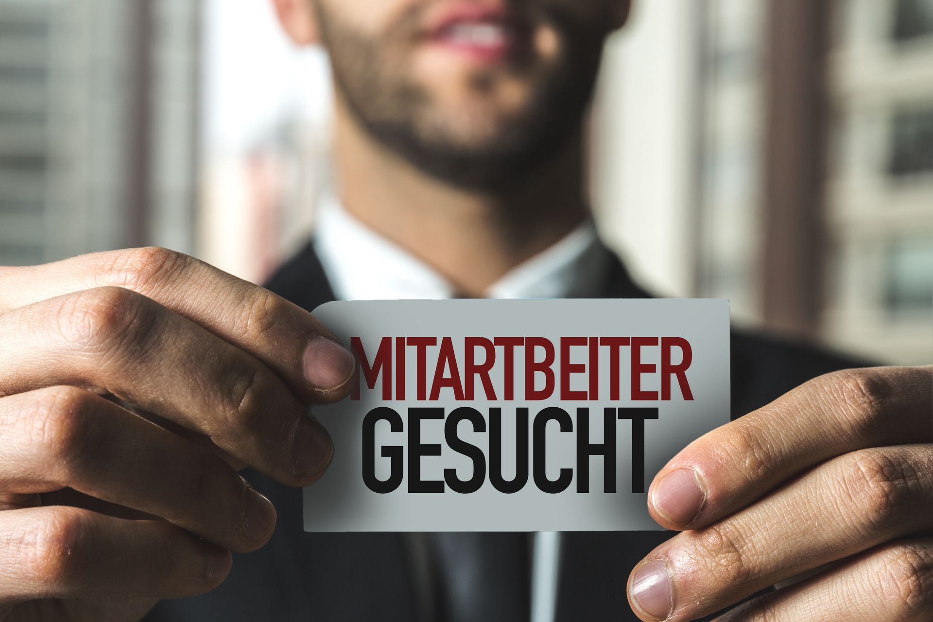 A man in a suit is holding a sign that says mitarbeiter gesucht