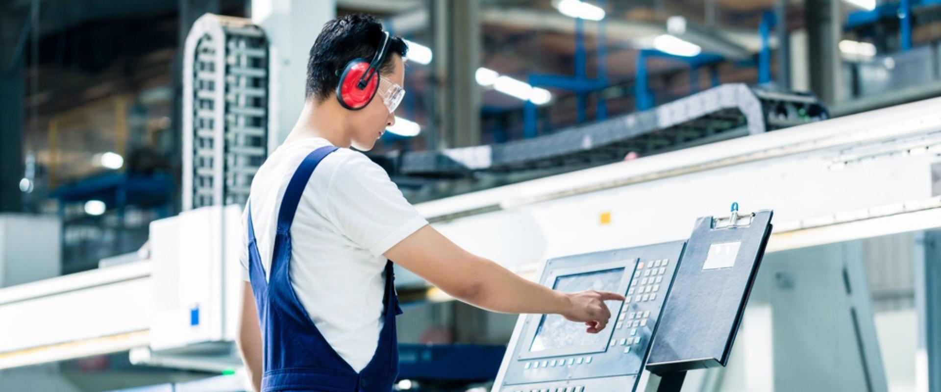 Ein Mann mit Kopfhörern arbeitet in einer Fabrik an einer Maschine.