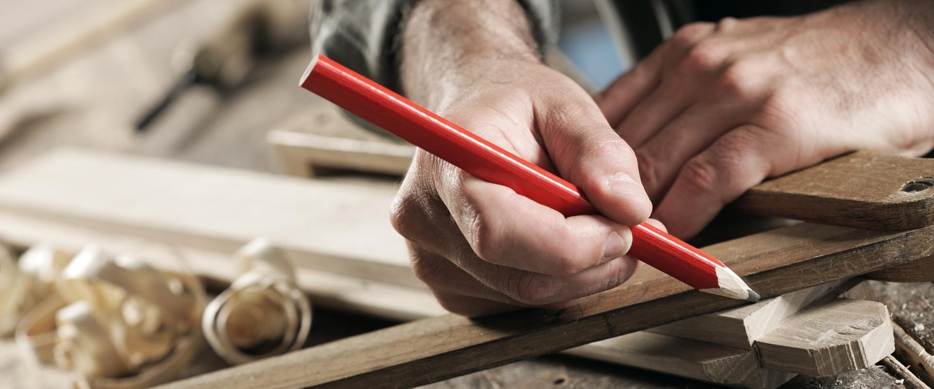 Eine Person misst ein Stück Holz mit einem roten Bleistift.